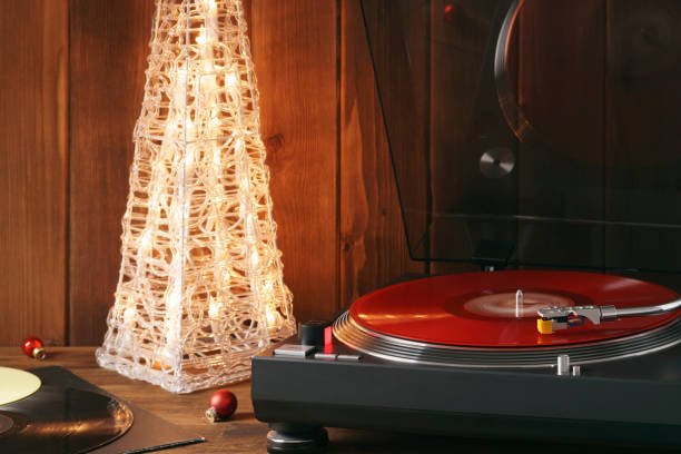 photo de noël. le moment tournant d'un disque vinyle rouge sur la platine, le stylet avec une aiguille tombe sur le vinyle, la musique sur le fond d'un arbre de noël lumineux avec des boules de verre rouge - christmas tree audio photos et images de collection