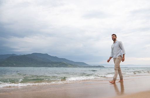 Peaceful man walking at the beach and looking very happy - wellness concepts