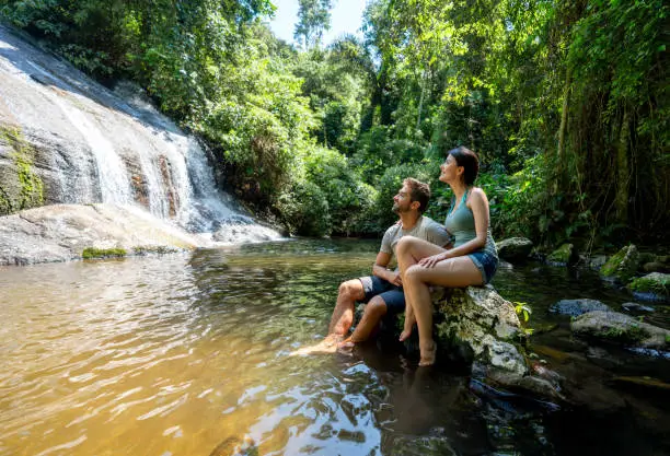 Happy couple of hikers looking at a beautiful waterfall in Brazil and smiling â outdoors lifestyle concepts