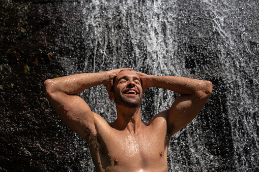 Portrait of a happy man enjoying the summer under a waterfall in Brazil â lifestyle concepts