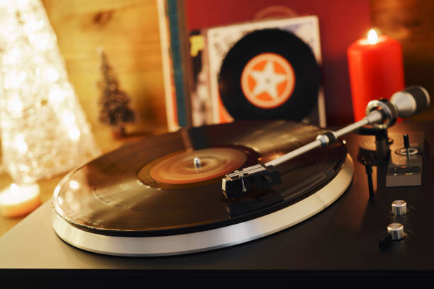 istock Turntable player with background of a stack of audition records and a Christmas tree. Sound technology DJ. Black vinyl record and stylus with needle. Christmas lights bokeh reflected on label surface 1135218149