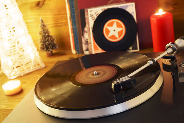istock Turntable player with background of a stack of audition records and a Christmas tree. Sound technology DJ. Black vinyl record and stylus with needle. Christmas lights bokeh reflected on label surface 1135218161