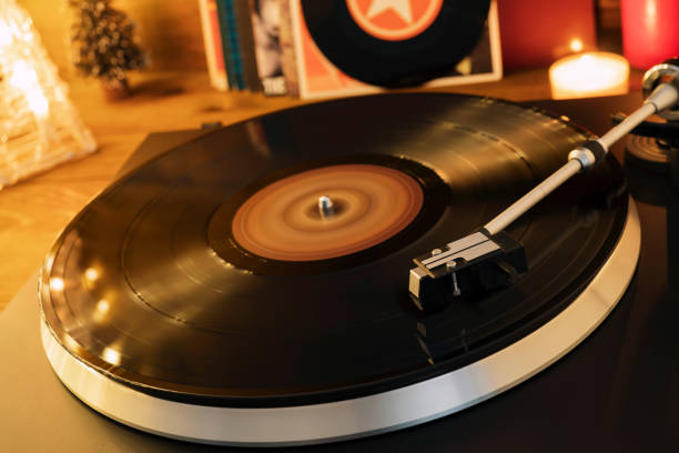 istock Turntable player with background of a stack of audition records and a Christmas tree. Sound technology DJ. Black vinyl record and stylus with needle. Christmas lights bokeh reflected on label surface 1135218165