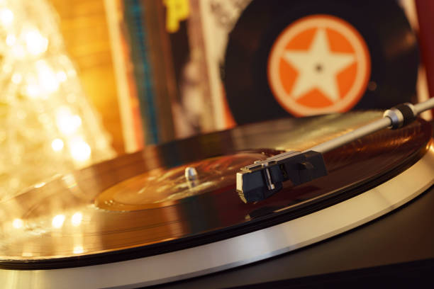 istock Turntable player with background of a stack of audition records and a Christmas tree. Sound technology DJ. Black vinyl record and stylus with needle. Christmas lights bokeh reflected on label surface 1135218168
