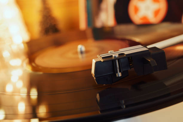 istock Turntable player with background of a stack of audition records and a Christmas tree. Sound technology DJ. Black vinyl record and stylus with needle. Christmas lights bokeh reflected on label surface 1135218169