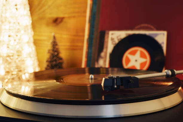 istock Turntable player with background of a stack of audition records and a Christmas tree. Sound technology DJ. Black vinyl record and stylus with needle. Christmas lights bokeh reflected on label surface 1135218175