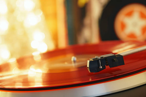 Turntable player with background of a stack of audition records and a Christmas tree. Sound technology DJ. Black vinyl record and stylus with needle. Christmas lights bokeh reflected on label surface