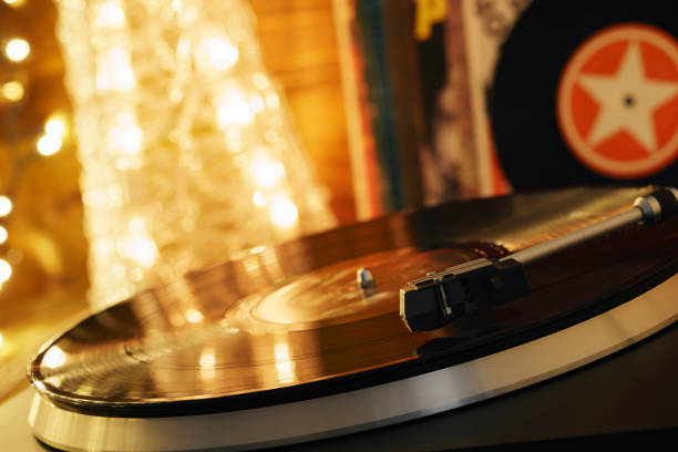 Turntable player with background of a stack of audition records and a Christmas tree. Sound technology DJ. Black vinyl record and stylus with needle. Christmas lights bokeh reflected on label surface