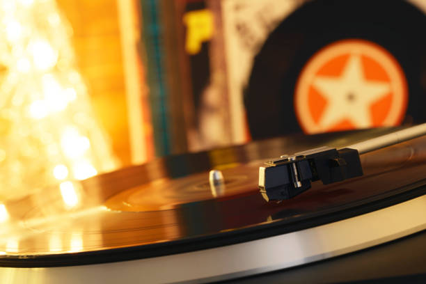 istock Turntable player with background of a stack of audition records and a Christmas tree. Sound technology DJ. Black vinyl record and stylus with needle. Christmas lights bokeh reflected on label surface 1135218185