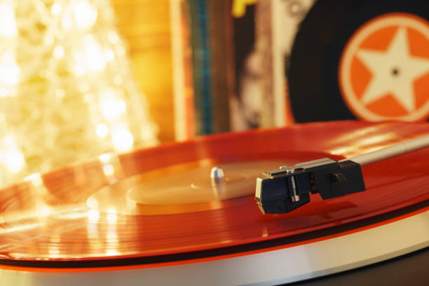 istock Turntable player with background of a stack of audition records and a Christmas tree. Sound technology DJ. Black vinyl record and stylus with needle. Christmas lights bokeh reflected on label surface 1135218192