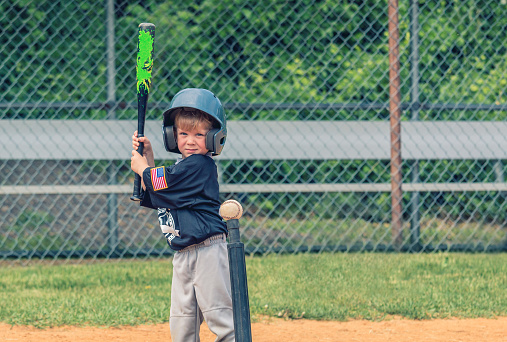 A little boy take a quick look at the camera prior to hitting a baseball from a tee.