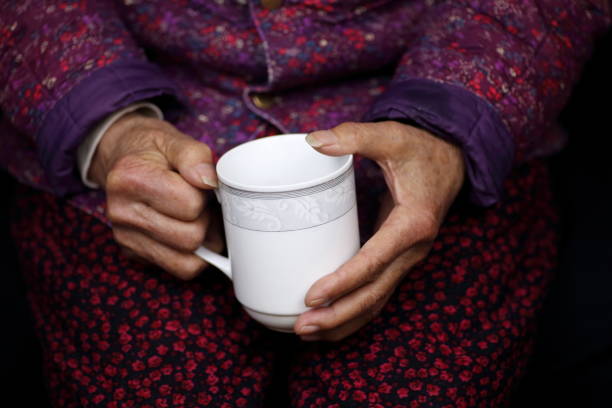 An elderly Chinese female sits and holds a tea cup.