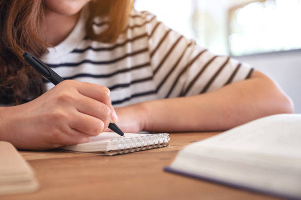 istock Closeup image of a woman writing on blank notebook with books on wooden table while learning 1135248259
