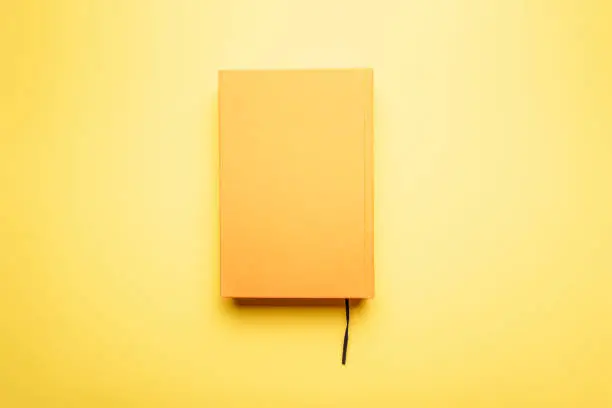 Photo of Read to the end of the literary work with a bookmark lies on a bright table. The book and the background is yellow.