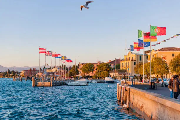 Sunset with red-yellow sun on a lake or sea. Sky, shore, sun and water. Flags of different cities, countries and territories. Free space for text