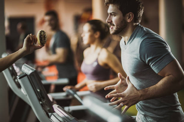 istock Athletic man running on treadmill while craving for sweet donut. 1135270424