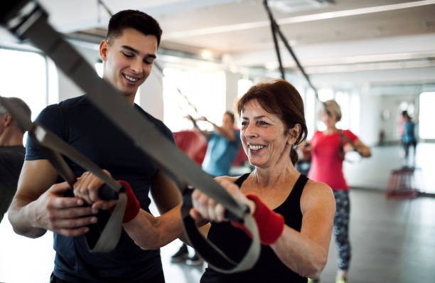 A group of cheerful seniors in gym with a young trainer doing exercise with TRX. A group of cheerful seniors in gym with a young personal trainer doing exercise with TRX. suspension training stock pictures, royalty-free photos & images