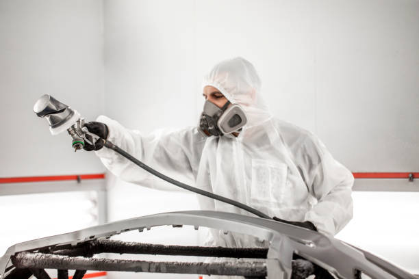 istock Car painter in white overalls spraying a small car part with paint 1135272935