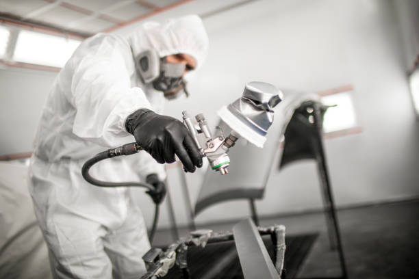 Professional car painting technician blasting small car parts on a stand with a coat of paint in a painting booth of a car body shop Car colorist in white protective suit blasting small car parts on a stand with a coat of paint in a painting booth of a car body shop. door panel stock pictures, royalty-free photos & images