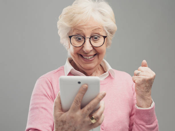 feliz sorpresa dama mayor usando una tableta digital - shaking fist fotografías e imágenes de stock