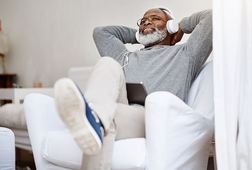 Shot of a handsome senior man listening to music on a tablet while relaxing on a couch at home