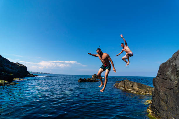 istock Two young men jumping off cliff into sea 1135281960
