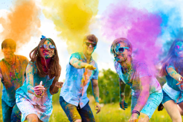Happy outdoor holi festival party in spring Cheerful and happy soiled friends throw bright paints on camera and smiling. Company of young people in sunglasses having fun with holi paints on spring summer festival. Holi party concept. holi stock pictures, royalty-free photos & images