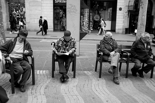 Barcelona, Spain - February 20, 2019: Spanish senior people reading newspapper and watching around on the bench inBarcelona, Spain.