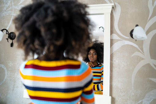 Rear view of african woman standing arms crossed and looking at her reflection in the mirror.