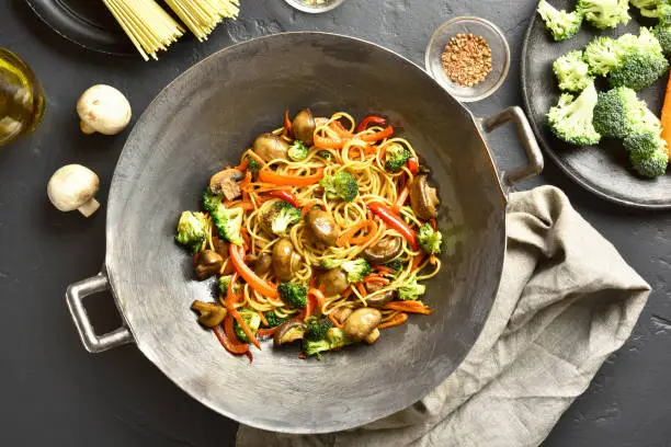 Stir-fry vegetables with noodles in wok pan on dark stone background. Top view, flat lay