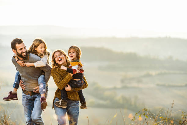 Young happy family enjoying in autumn walk on a hill. Happy parents and their small kids taking an autumn walk on the field. Father is piggybacking daughter. Copy space. happy family stock pictures, royalty-free photos & images