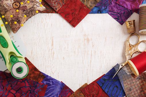 Quilting accessories forming a heart shape on a white wooden surface