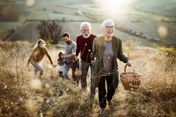 Photo of Happy senior woman leading her family to perfect picnic place on the hill.