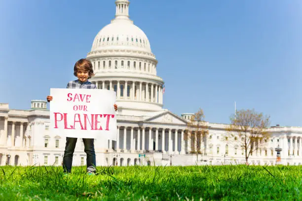 Child boy protest in front of the USA capitol in Washington holding sign saying save our planet
