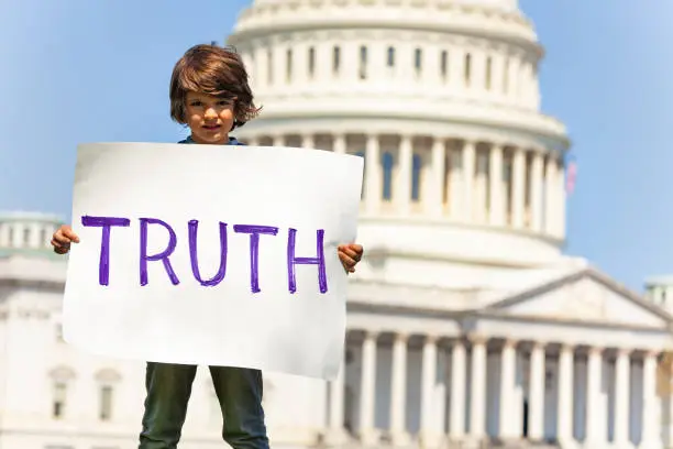 Child boy protest in front of the USA capitol in Washington holding sign saying  truth
