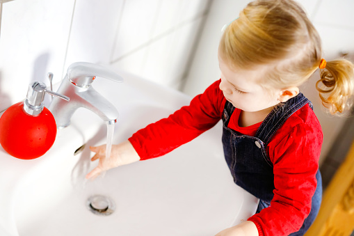 Cute little toddler girl washing hands with soap and water in bathroom. Adorable child learning cleaning body parts. Morning hygiene routine. Happy healthy kid at home or nursery