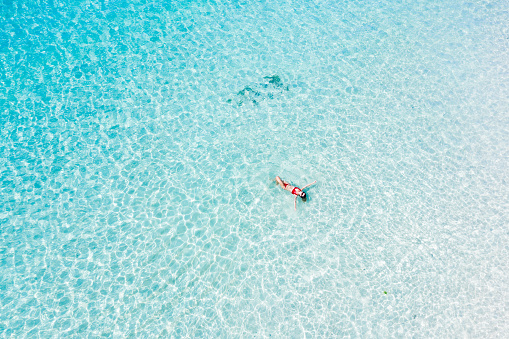 Woman floating in transparent turquoise ocean. View from above.