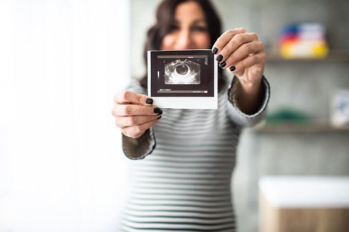 Pregnant woman holding and showing ultrasound picture of her baby, focus on foreground