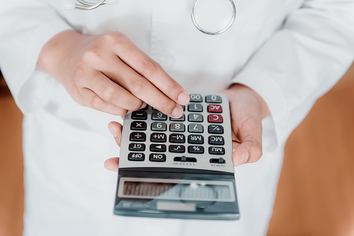 Close-Up of Female Doctor is Calculating Medicine Cost in Office Hospital, Female Medical is Using Calculator. Healthcare and Financial Concept.