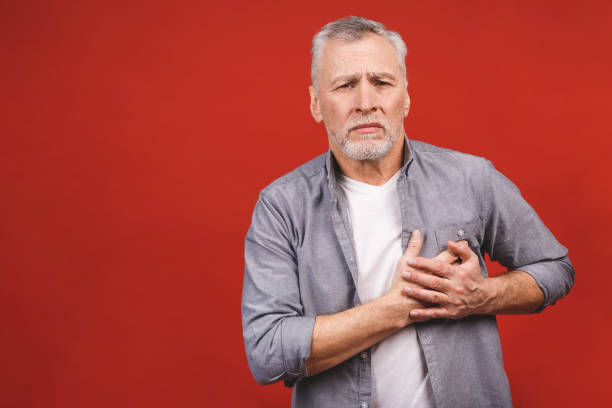 Seniour aged man having chest pain isolated against red background. Health lifestyle concept. Seniour aged man having chest pain isolated against red background. Health lifestyle concept. male chest pain stock pictures, royalty-free photos & images