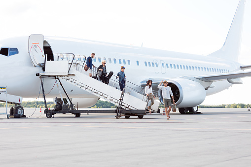 Group of passengers disembarking the airplane. People getting off a plane.