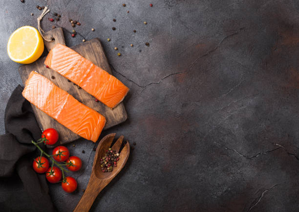 istock Fresh raw salmon slice on chopping board with pepper tomatoes and lemon on stone kitchen table background. Space for text. With rosemary and salt 1135324264