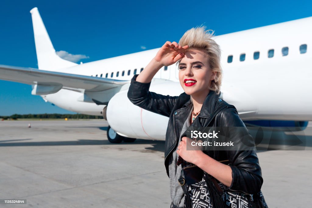 Attractive young woman at airport Portrait of attractive young woman outdoors at airport. Stylish woman walking in front of a plane and looking away. Adult Stock Photo