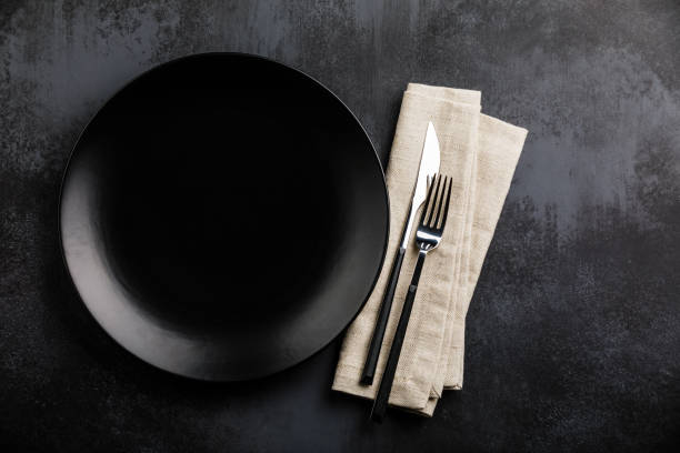impostazione del tavolo con piatto nero vuoto, posate a forchetta e coltello e tovagliolo di lino su tavolo scuro - table knife silverware black fork foto e immagini stock