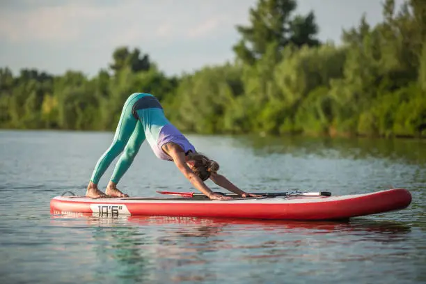 Photo of Young woman are doing yoga on a stand up paddle board SUP on a beautiful lake or river