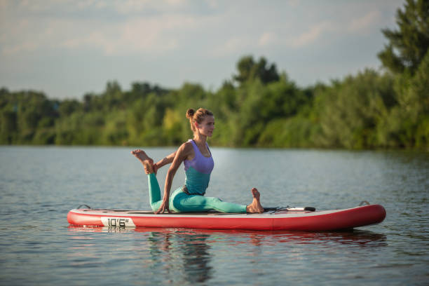 giovane donna che fa yoga a bordo sup board con pagaia. posa meditativa, vista laterale - concetto di armonia con la natura - paddleboard oar women lake foto e immagini stock