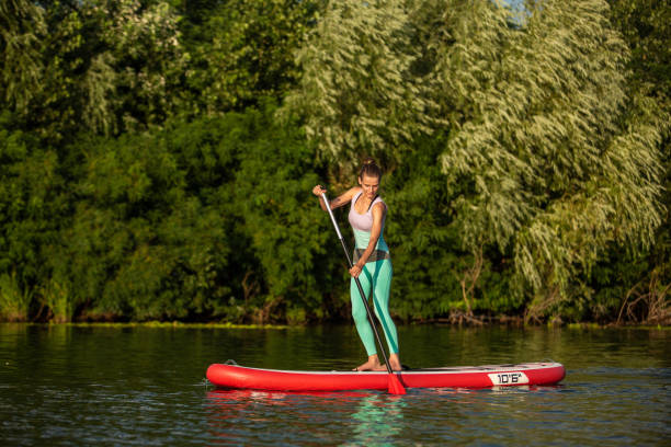 mujer atlética joven haciendo fitness en un tablero con un remo en un lago. - paddleboard oar women lake fotografías e imágenes de stock