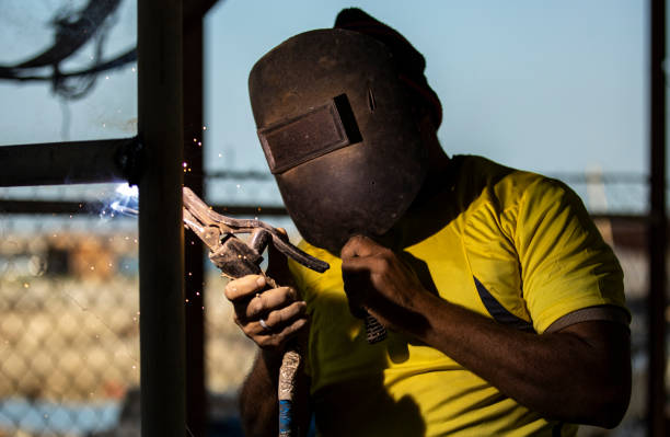 trabajador de soldadura de una valla polos juntos, sosteniendo una máscara de soldadores con otra mano para proteger su cara - indian ocean flash fotografías e imágenes de stock