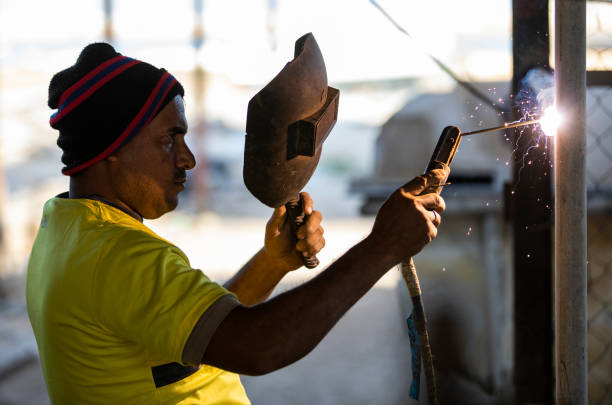 trabajador de soldadura de una valla polos juntos, sosteniendo una máscara de soldadores con otra mano para proteger su cara - indian ocean flash fotografías e imágenes de stock