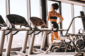 Young sporty muscular brunette with ponytail running on treadmill. Backs turned, full length. You can't always wait for the perfect time, sometimes you must dare to jump.